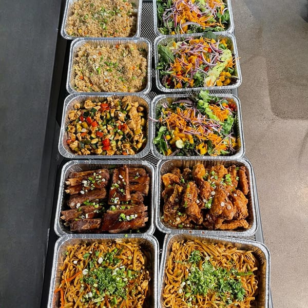 A catering spread of Asian-fusion dishes including fried rice, salads, ribs, fried chicken, and noodles.