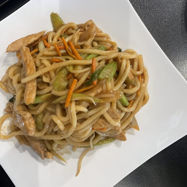 Udon noodles with chicken, carrots, and green onions on a white rectangular plate.