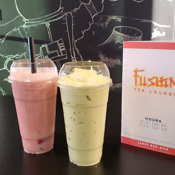 Two Fusion Tea Lounge smoothies, one pink and one green, with a menu card on a dark table.