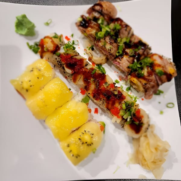 A white plate with two rows of sushi rolls, one topped with kiwi and the other with seared meat.