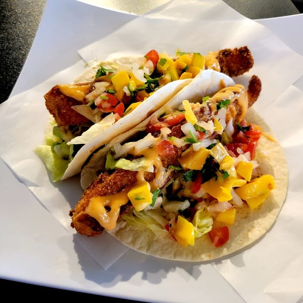 Two Fusion Tea Lounge fish tacos with crispy fish, mango salsa, and sauce on a white plate.
