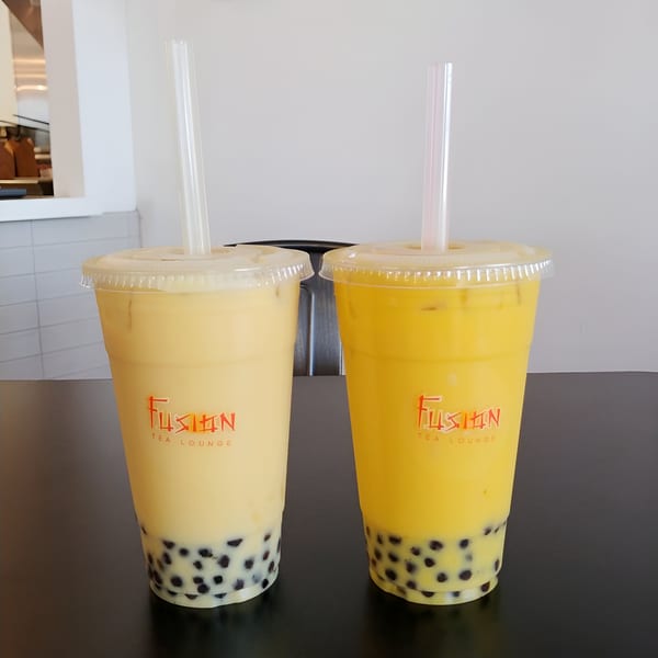 Two Fusion Tea Lounge bubble teas, one light yellow and one bright yellow, with tapioca pearls.