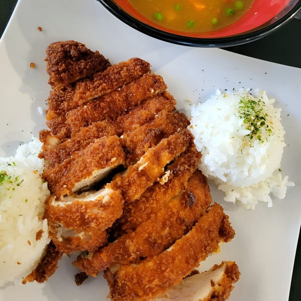 Crispy golden-brown chicken katsu, sliced and served with white rice and a side of soup.